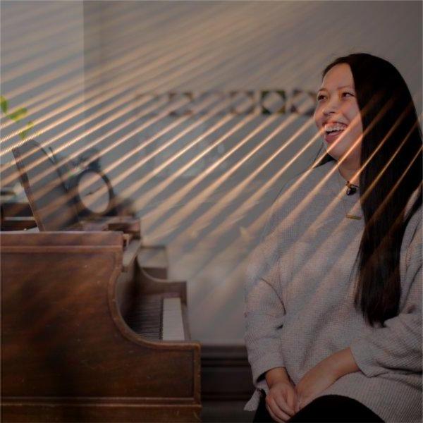 A person sitting at a piano smiles as filtered sunlight beams through.
